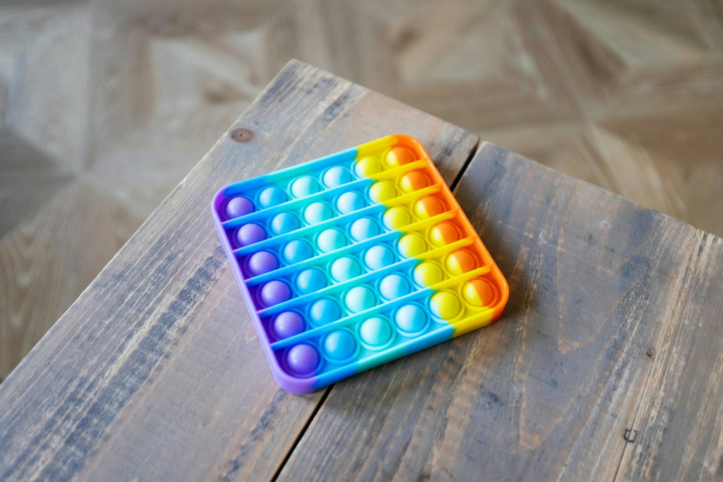 A rainbow colored silicone fidget toy rests on wooden boards.